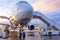 Nose view of an airplane with gangway for boarding parked at an airport during sunset bright light shine and clouds in the sky