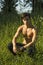 Nostalgic shirtless young man in a park as he kneels in green grass