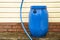 Not so high blue plastic rainwater barrel stands outside near the wall. It is used for watering.