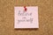 Note with phrase Believe In Yourself pinned on corkboard. Motivational quote