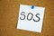 Note with SOS inscription. Sticky note with SOS inscription pinned on a cork bulletin board