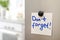 Note with text `Don`t forget` and magnet on refrigerator door in kitchen