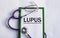 Notebook pade with word LUPUS, on a table with a stethoscope