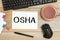 Notebook with text OSHA - Occupational Safety and Health Administration, near office supplies