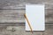 Notepad with a blank white sheet in a checker paper with simple graphite pencil lies on the background of wooden boards