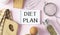 Notepad with Diet Plan list text on chopping board with wooden fork and spoon and measuring tape on pink table , recipes food