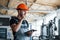 With notepad in hands. Industrial worker indoors in factory. Young technician with orange hard hat