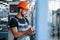 With notepad in hands. Industrial worker indoors in factory. Young technician with orange hard hat