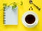 Notepad for notes, green leaves plant coffee Cup on yellow desktop, flat lay, copy space.