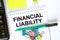 Notepad with text Financial Liability. Calculator, green pen stickers and stationary clips