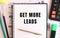 Notepad with text GET MORE LEADS on the office desk, near office supplies. Business concept