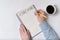 Notepad with word COACHING. Female hands and cup of coffee on white background. Top view