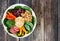 Nourishment bowl with quinoa, hummus, mixed vegetables, over rustic wood