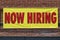 Now Hiring bright yellow banner sign with red print I