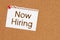 Now hiring message on card on a corkboard