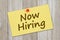 Now hiring message on retro yellow paper index card with pushpin