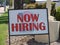 A Now Hiring Sign Goes Up On A Busy Street