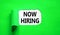 Now hiring symbol. Concept words Now hiring on beautiful white paper. Beautiful green table green background. Business marketing,