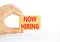 Now hiring symbol. Concept words Now hiring on beautiful wooden block. Beautiful white table white background. Businessman hand.