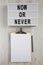 `Now or never ` word on modern board, clipboard with sheet of paper on a white wooden background, top view. Space for text