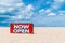 Now open sign board stand on sand summer beach background metaphor to time to travel relax tourism season with copyspace