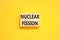 Nuclear fission symbol. Concept words Nuclear fission on beautiful wooden blocks. Beautiful yellow table yellow background.