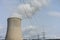 Nuclear power plant chimney with condensation smoke on a cloudy day with power pole electricity tower in the back