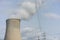 Nuclear power plant chimney with condensation smoke on a cloudy day with power pole electricity tower in the back