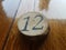 The number 12 on a circular piece of wood on a waxed wooden table