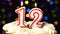 Number 12 on top of cake - twelve birthday candle burning - blow out at the end. Color blurred background