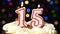 Number 15 on top of cake - fifteen birthday candle burning - blow out at the end. Color blurred background