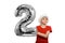 Number 2 of a silver balloon in the hands of a blond boy in a red Santa hat. White background