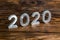 A number 2020 with white metal digits on dark brown wood background with selective focus