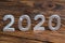 A number 2020 with white metal digits on dark brown wood background with selective focus
