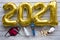 Number 2021 made from golden inflated balloons on a rustic wooden table along with coronavirus prevention medical devices. Happy