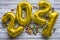 Number 2021 made from golden inflated balloons on a rustic wooden table along with small and sweet chocolates. Happy new year