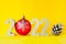 Number 2022 with concrete numbers and a Christmas tree ball on a yellow background with a fir cone