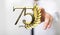 Number 75 and spikes of wheat over a person\'s fingers