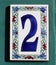 number two ceramic sign made of enamel or clay on a turquoise wooden wall, 2 with flowers
