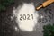 Numbers 2021 handwritten on flour with christmas cookie cutters, rolling pin and pine branches on dark background