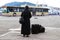 Nun traveling with suitcases and luggage. A woman in black monastic clothes is waiting for a bus on the waterfront of the old