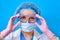 A nurse on a blue background adjusts medical goggles on her face. Doctor in a protective mask and clothing for the treatment of