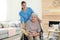 Nurse covering elderly woman in wheelchair with blanket. Assisting senior people