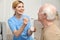 Nurse feeding elderly man with yogurt. Assisting senior people