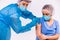 A nurse in protective equipment, in a medical mask, makes a young woman doctor a vaccine for covid 19 and looks at the