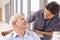 Nurse Pushing Senior Patient In Wheelchair Along Corridor