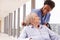 Nurse Pushing Senior Patient In Wheelchair Along Corridor