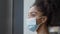 Nurse In Scrubs With Face Mask Looking Out Of Window In Busy Hospital During Health Pandemic