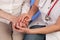 Nurse with stethoscope lovingly holds hands of elderly woman