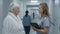 Nurse with tablet and elderly woman talk, walk along the clinic corridor